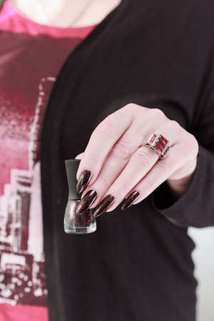 Female hands with long nails and black and red manicure holding a bottle of nail polishの写真素材