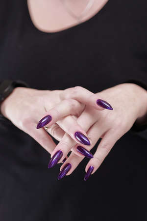 Female hand with long nails and dark purple manicure holds a bottle of nail polishの写真素材