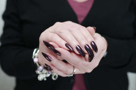 Female hand with long nails and dark purple manicure holds a bottle of nail polishの写真素材