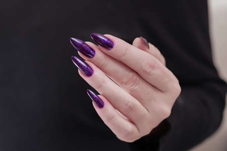 Female hand with long nails and purple plum manicure holds a bottle of nail polish