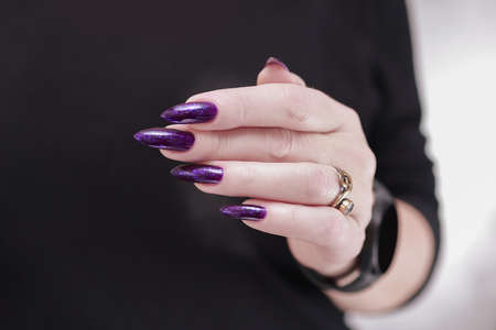 Female hand with long nails and purple plum manicure holds a bottle of nail polishの写真素材