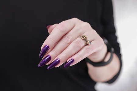 Female hand with long nails and purple plum manicure holds a bottle of nail polishの写真素材