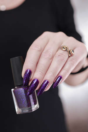 Female hand with long nails and purple plum manicure holds a bottle of nail polish