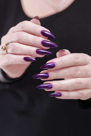 Female hand with long nails and purple plum manicure holds a bottle of nail polishの写真素材