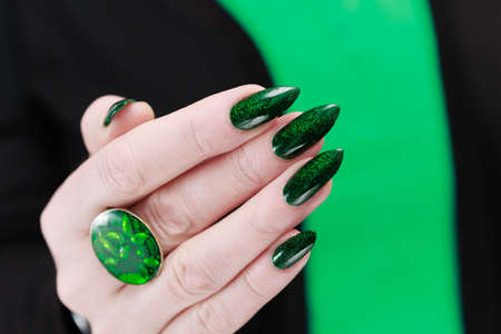 Woman's hand with long nails and bright green manicure with bottles of nail polish