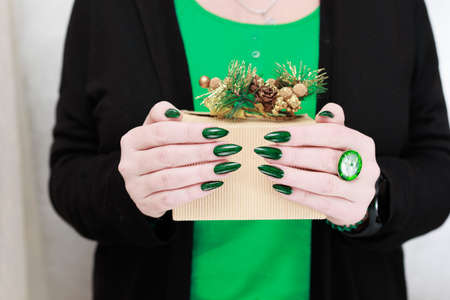 Female hands with green manicure hold a gift box for New Year and Christmas.