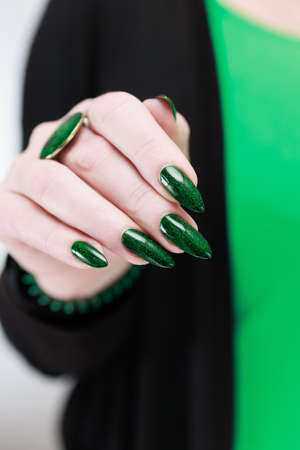 Woman's hand with long nails and bright green manicure with bottles of nail polishの写真素材