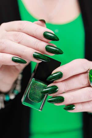 Woman's hand with long nails and bright green manicure with bottles of nail polishの写真素材