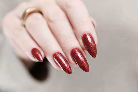 Female hand with long nails and a red manicure holds a bottle of nail polishの写真素材