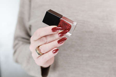 Female hand with long nails and a red manicure holds a bottle of nail polish