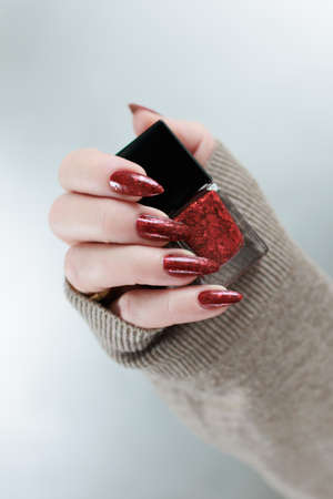Female hand with long nails and a red manicure holds a bottle of nail polish