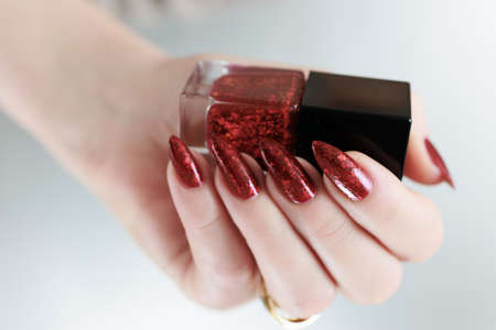 Female hand with long nails and a red manicure holds a bottle of nail polish