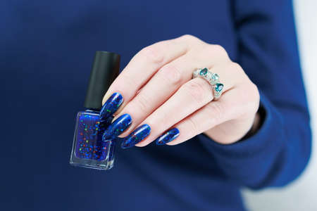 Woman's beautiful hand with long nails and bright blue manicure with bottles of nail polish