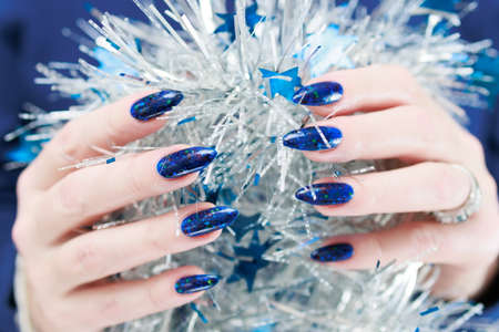 Women's hands with long nails and bright blue manicure hold a silver garland. Congratulations to the New Year and Christmas.の写真素材