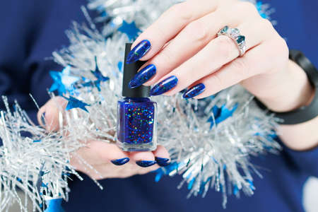 Women's hands with long nails and bright blue manicure hold a silver garland. Congratulations to the New Year and Christmas.の写真素材
