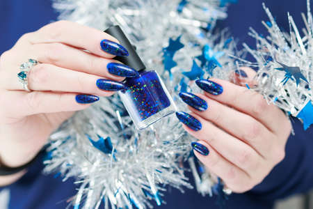 Women's hands with long nails and bright blue manicure hold a silver garland. Congratulations to the New Year and Christmas.の写真素材