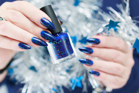 Women's hands with long nails and bright blue manicure hold a silver garland. Congratulations to the New Year and Christmas.の写真素材