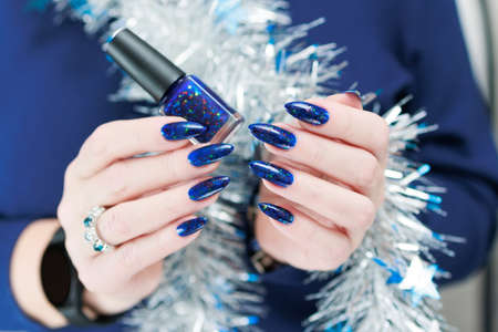 Women's hands with long nails and bright blue manicure hold a silver garland. Congratulations to the...