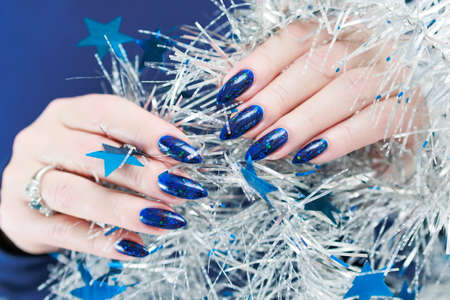 Women's hands with long nails and bright blue manicure hold a silver garland. Congratulations to the New Year and Christmas.の写真素材