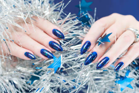 Women's hands with long nails and bright blue manicure hold a silver garland. Congratulations to the New Year and Christmas.の写真素材