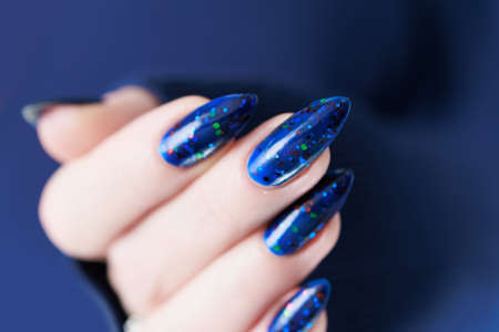 Woman's beautiful hand with long nails and bright blue manicure with bottles of nail polish