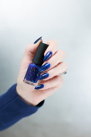 Woman's beautiful hand with long nails and bright blue manicure with bottles of nail polish