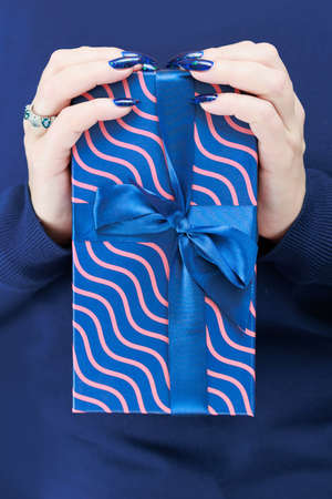 Female hands with long nails hold a gift box in blue colors