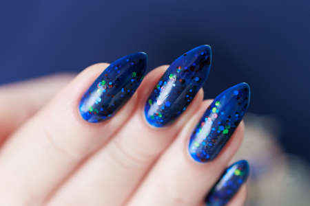 Woman's beautiful hand with long nails and bright blue manicure with bottles of nail polish