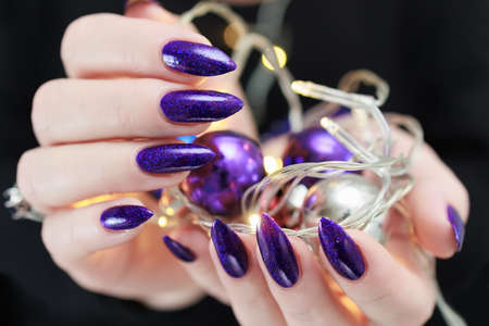 Female hands with long nails and bright purple and blue manicure hold a gift box and Christmas...
