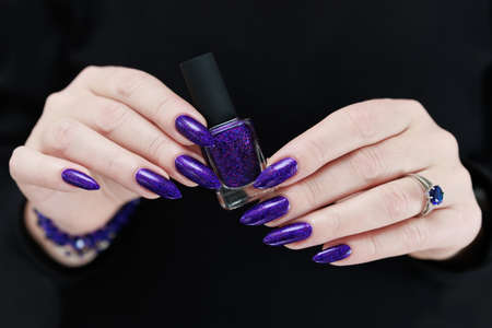 Female hand with long nails and purple plum manicure holds a bottle of nail polish