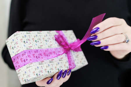 Female hands with long nails hold a gift box in purple colors