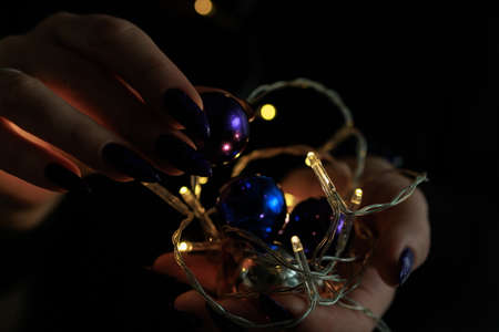 Female hands with long nails and bright purple and blue manicure hold a gift box and Christmas...