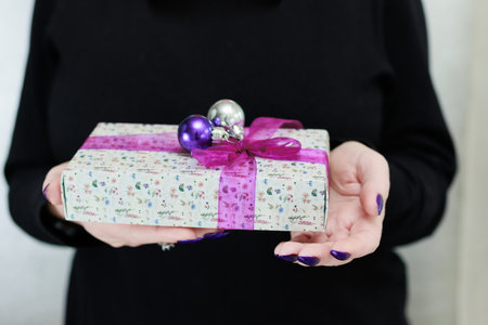 Female hands with long nails and bright purple and blue manicure hold a gift box and Christmas balls. Congratulations to the New Year and Christmas.の写真素材