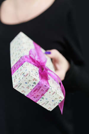 Female hands with long nails hold a gift box in purple colors