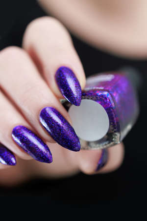 Female hand with long nails and purple plum manicure holds a bottle of nail polish