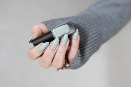 Female hand with long nails and gray green manicure with bottles of nail polishの写真素材