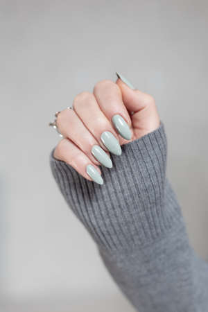 Female hand with long nails and gray green manicure with bottles of nail polish