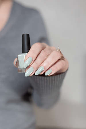 Female hand with long nails and gray green manicure with bottles of nail polishの写真素材