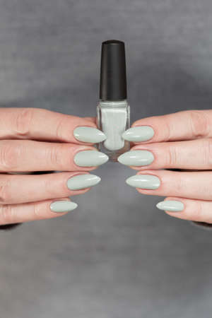 Female hand with long nails and gray green manicure with bottles of nail polishの写真素材