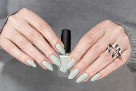 Female hand with long nails and gray green manicure with bottles of nail polish
