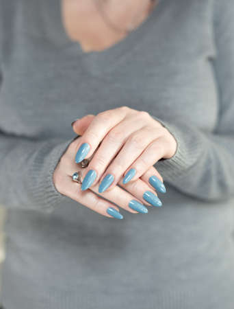Woman's beautiful hand with long nails and light blue manicure with bottles of nail polishの写真素材