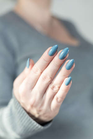 Woman's beautiful hand with long nails and light blue manicure with bottles of nail polish