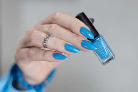 Woman's beautiful hand with long nails and light blue manicure with bottles of nail polish