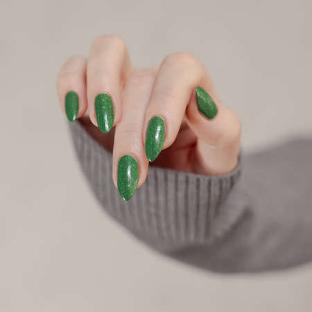 Woman's hand with long nails and green manicure with bottles of nail polishの写真素材