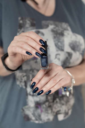 Female hand with long nails and dark blue teal manicure holds a bottle of nail polishの写真素材