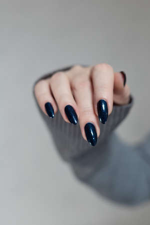 Female hand with long nails and dark blue teal manicure holds a bottle of nail polishの写真素材
