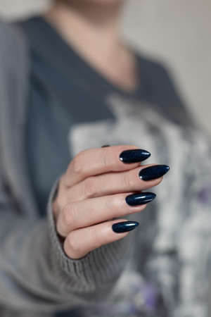 Female hand with long nails and dark blue teal manicure holds a bottle of nail polishの写真素材