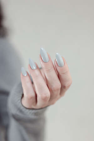 Female hand with long nails and a gray manicure holds a bottle of nail polishの写真素材