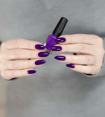 Female hand with long nails and a bottle of light blue lilac color nail polishの写真素材