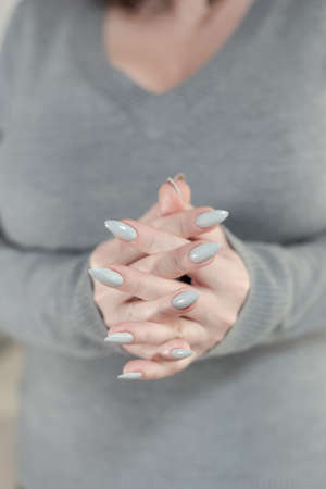Female hand with long nails light gray manicure and a bottle of nail polish